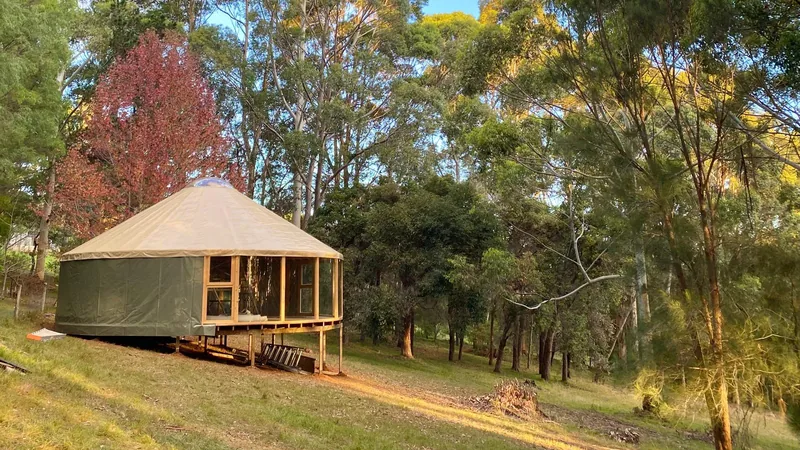 An ORON with green walls and a sand coloured roof on a raised platform among tall gums