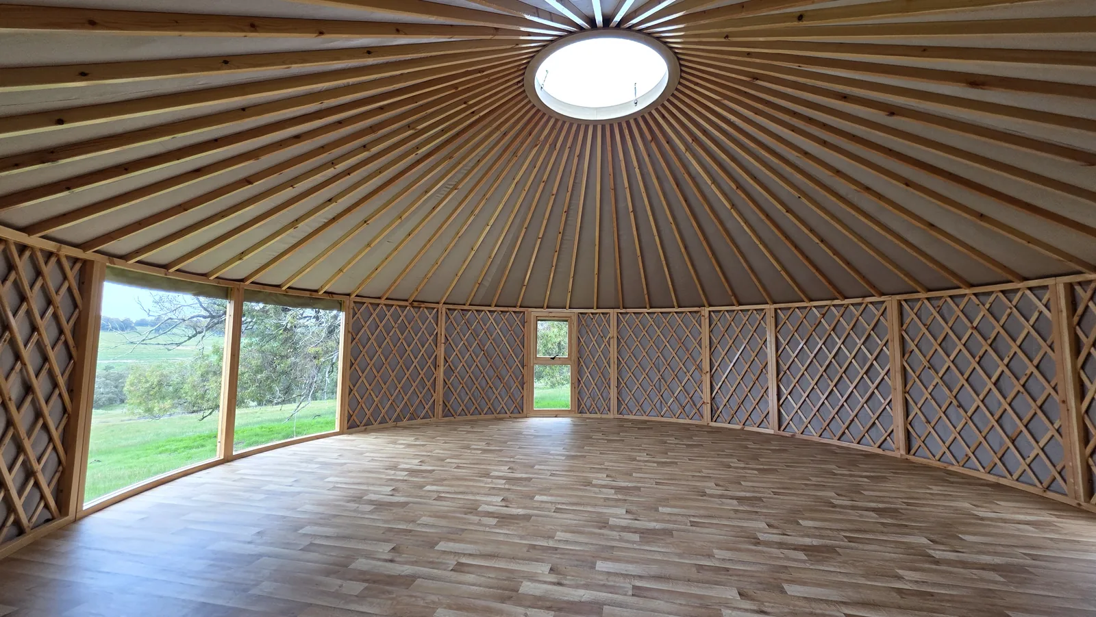 Inside an empty 8m ORON, looking out through a wide curved glass bay window and a full-height window to green paddocks