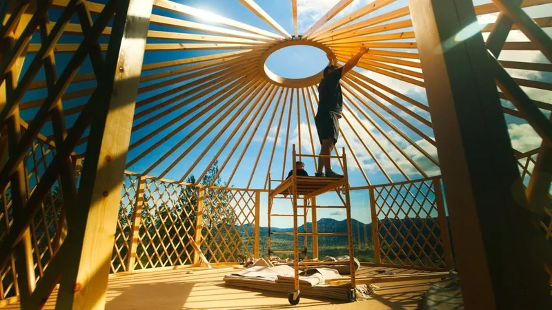 An ORON frame going up, with a builder on scaffolding fitting the crown ring and mountains visible through the lattice walls