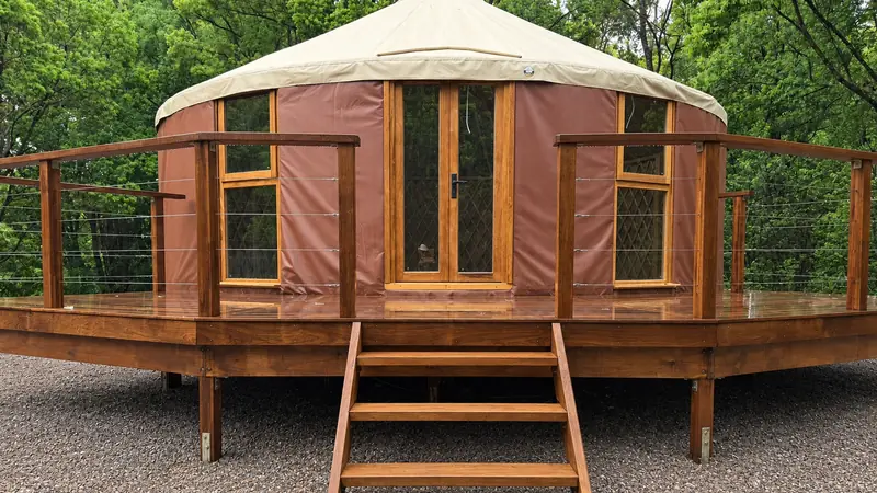 An ORON yurt with red ochre walls and a sand coloured roof on a raised hardwood deck