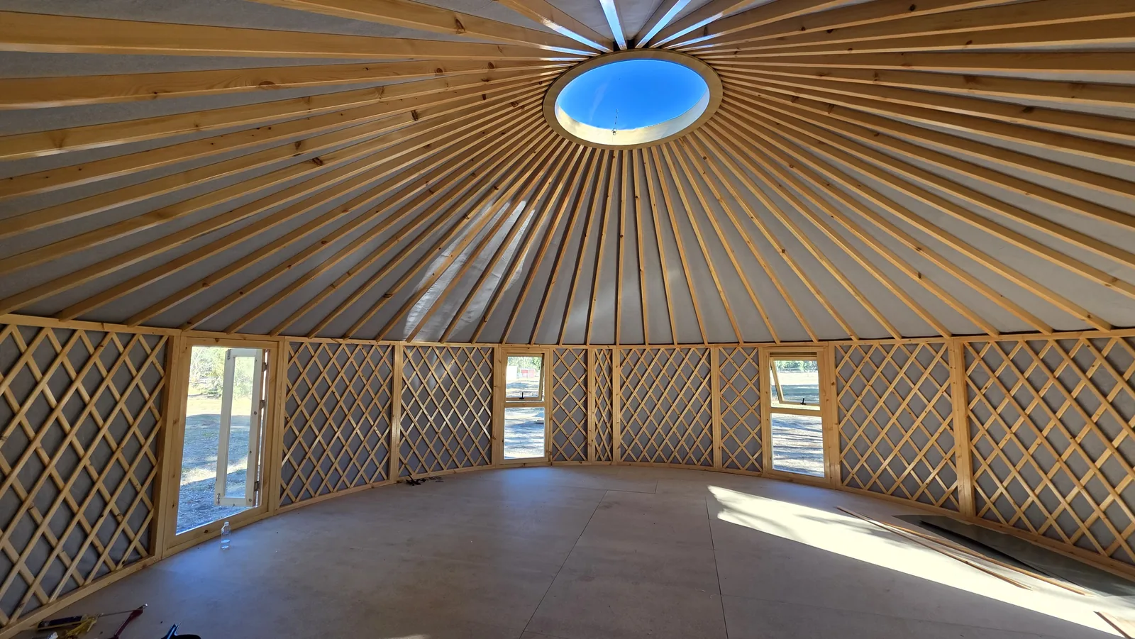 Tanya's empty 8m ORON interior with pale timber lattice walls, pine rafters, a ring of windows and afternoon sun across the floor
