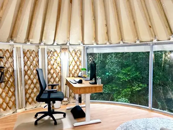 White yurt with a covered timber deck and outdoor furniture in bushland