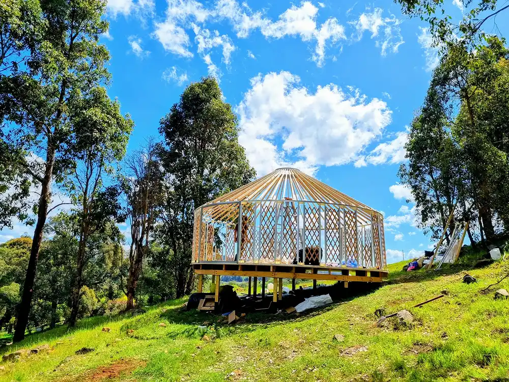 White yurt with glass doors on a timber deck in a green paddock